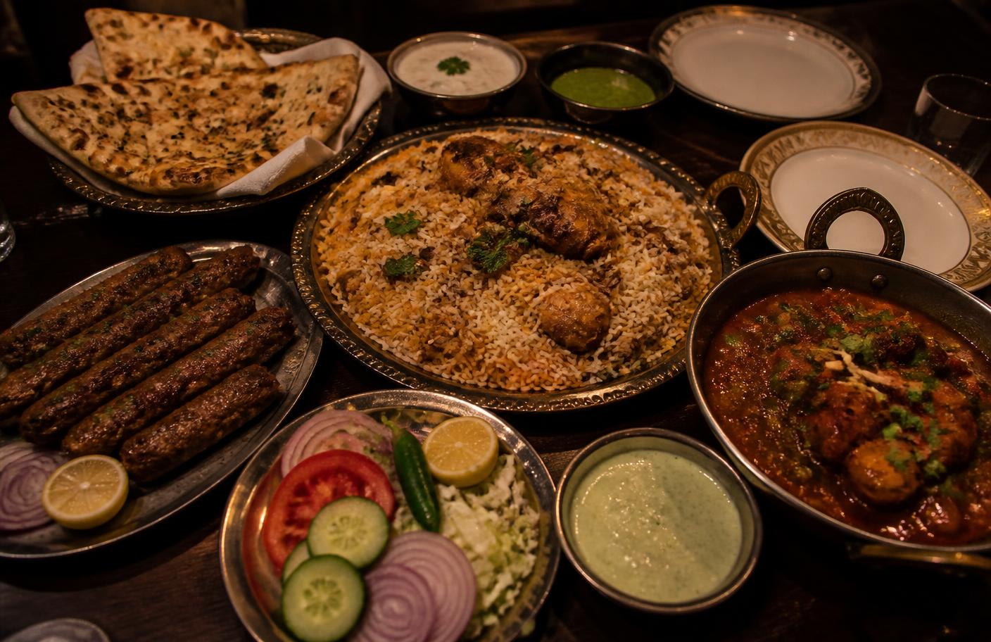 Pakistani family-style dinner spread with biryani, karahi, naan, kebabs, raita and salad